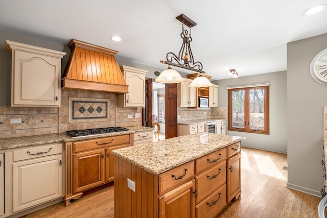 kitchen featuring appliances with stainless steel finishes, a kitchen island, light wood-style floors, and custom range hood