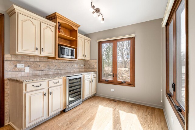 kitchen with stainless steel microwave, wine cooler, cream cabinetry, and open shelves