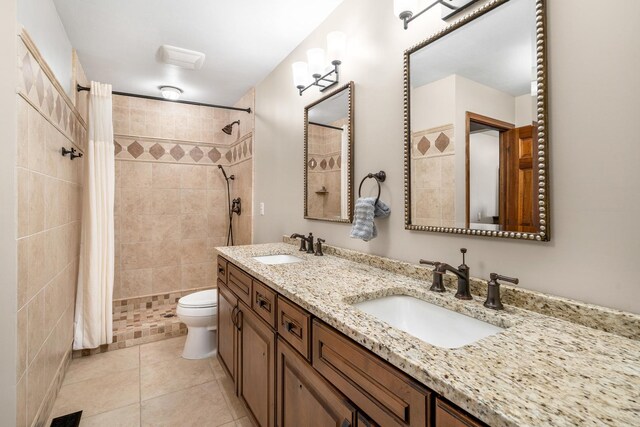 full bathroom featuring a tile shower, tile patterned flooring, double vanity, and a sink