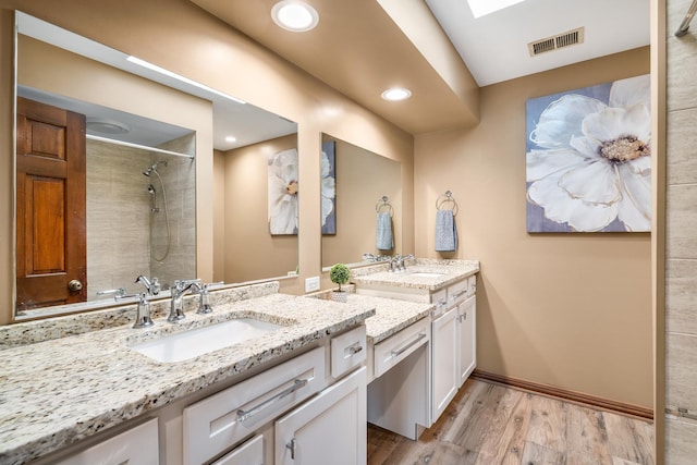 full bath featuring a sink, visible vents, tiled shower, and wood finished floors