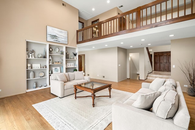 living room featuring light wood finished floors, visible vents, stairs, and a high ceiling