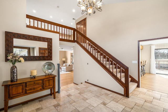 staircase featuring visible vents, a notable chandelier, stone tile floors, a high ceiling, and baseboards