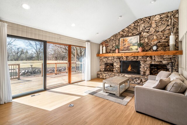 living area featuring light wood finished floors, a stone fireplace, lofted ceiling, and visible vents