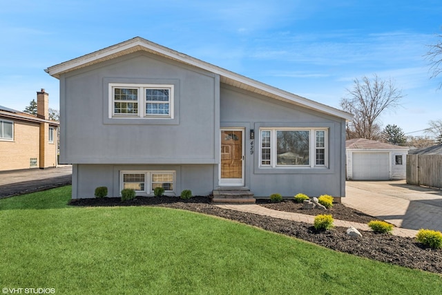 split level home with stucco siding, entry steps, an outdoor structure, a front yard, and a garage