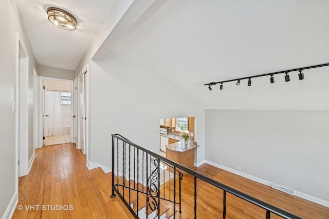 hall with visible vents, an upstairs landing, light wood-style flooring, rail lighting, and baseboards