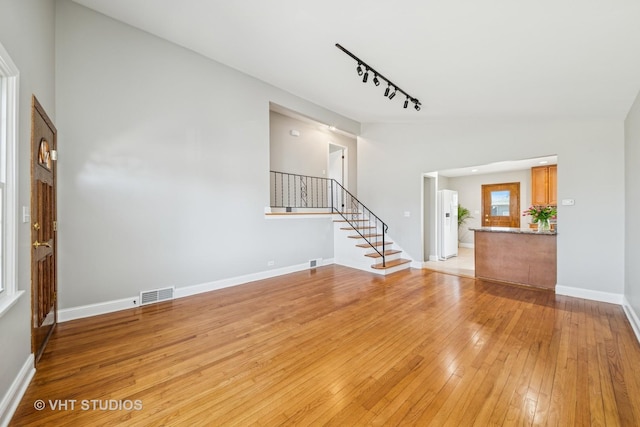 unfurnished living room with visible vents, baseboards, stairway, lofted ceiling, and light wood-style floors