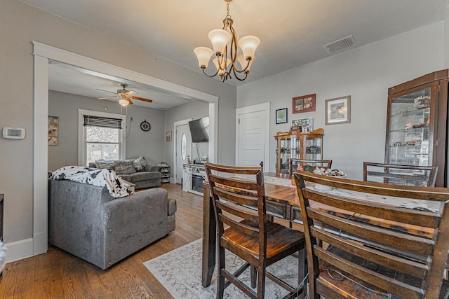 dining space featuring ceiling fan with notable chandelier, wood finished floors, visible vents, and baseboards