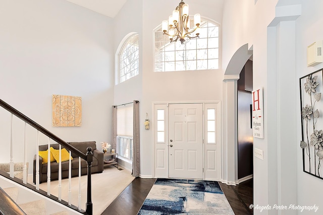 entryway featuring arched walkways, a notable chandelier, a high ceiling, and dark wood finished floors