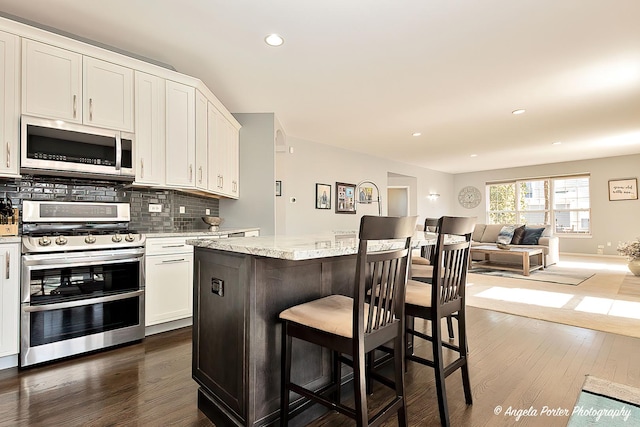 kitchen with dark wood-type flooring, tasteful backsplash, open floor plan, white cabinetry, and appliances with stainless steel finishes