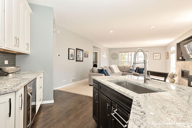 kitchen with a sink, wine cooler, open floor plan, white cabinetry, and tasteful backsplash