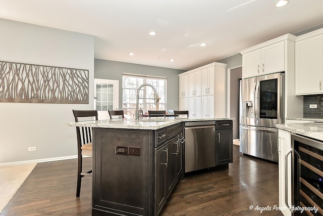 kitchen with beverage cooler, a kitchen bar, appliances with stainless steel finishes, white cabinetry, and a sink