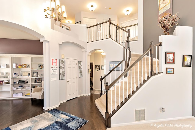 foyer entrance with wood finished floors, a high ceiling, visible vents, and arched walkways