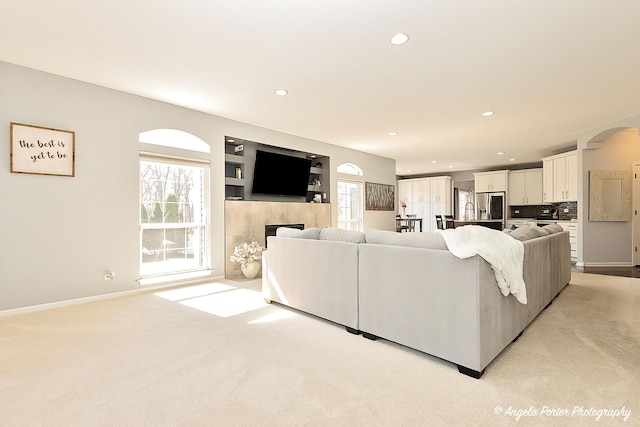 living room with baseboards, a fireplace, recessed lighting, arched walkways, and light carpet