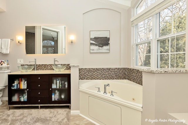 bathroom featuring double vanity, toilet, a jetted tub, and a sink