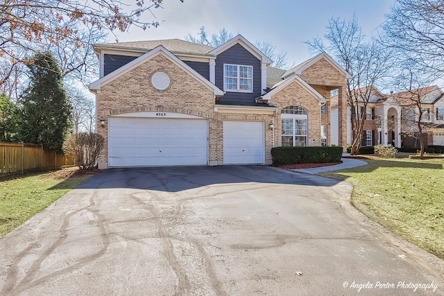 traditional-style home with brick siding, an attached garage, a front lawn, fence, and driveway