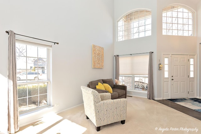 carpeted entrance foyer featuring a high ceiling, baseboards, and visible vents