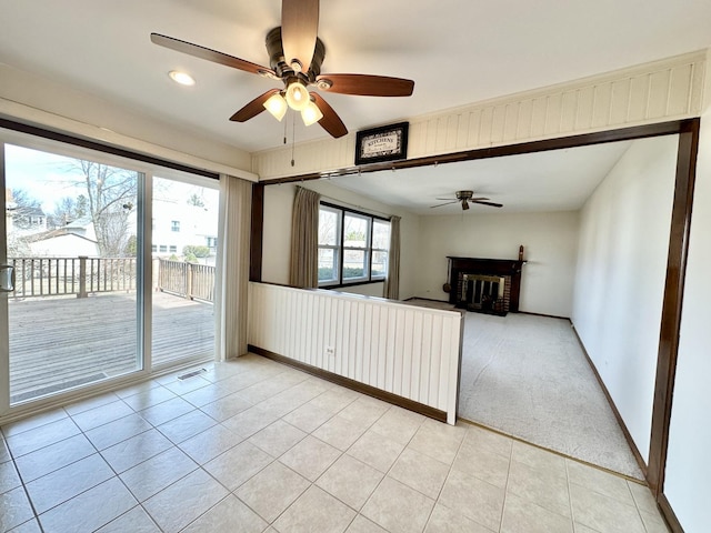 spare room with a ceiling fan, visible vents, light tile patterned flooring, a fireplace, and light colored carpet