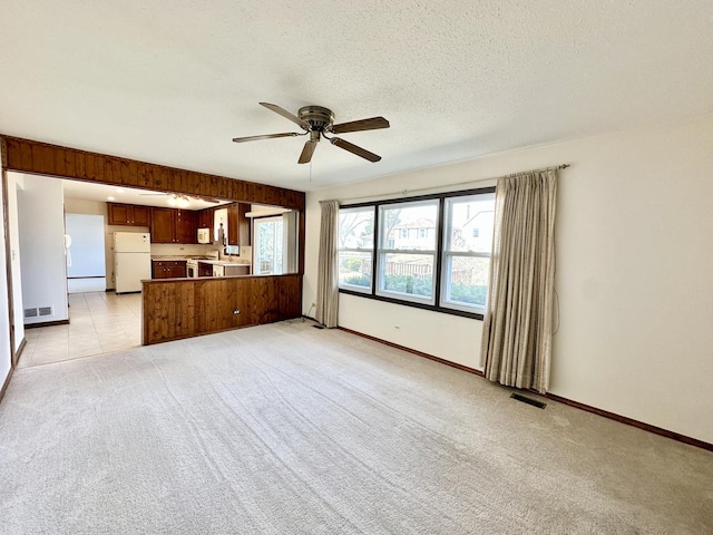 unfurnished living room featuring visible vents, baseboards, ceiling fan, light colored carpet, and a textured ceiling