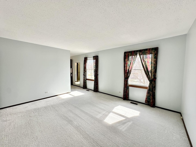 unfurnished room with baseboards, carpet, visible vents, and a textured ceiling