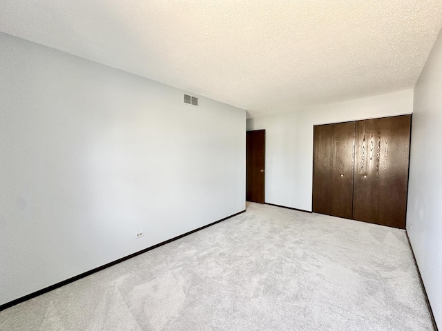 unfurnished bedroom with visible vents, light carpet, a textured ceiling, and a closet