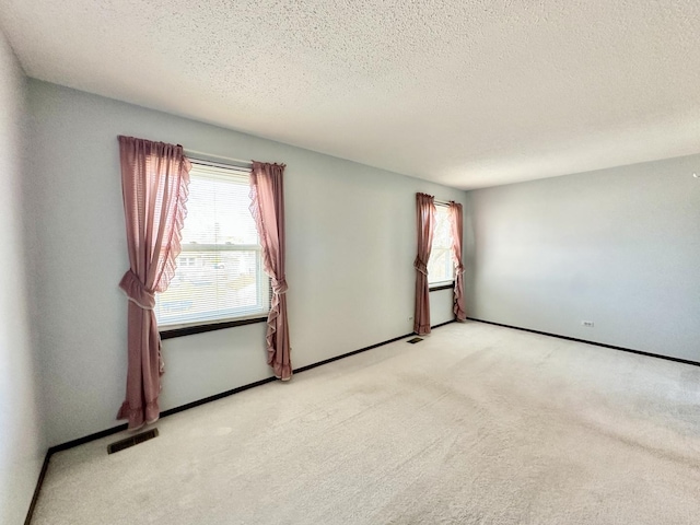 spare room featuring light carpet, visible vents, a textured ceiling, and baseboards