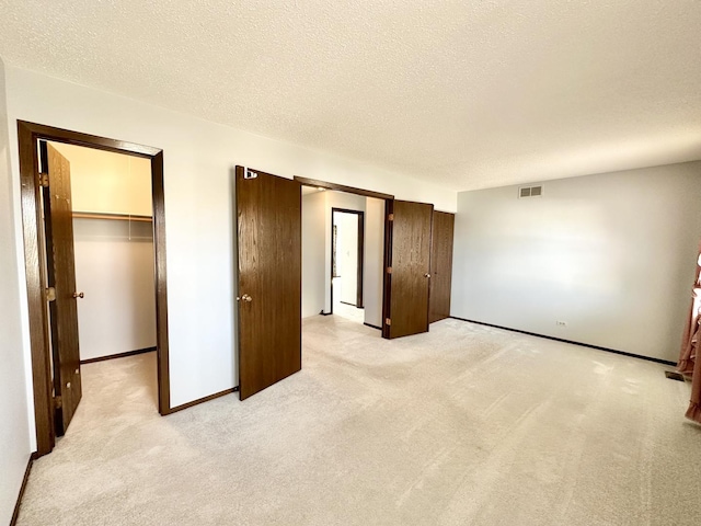 interior space with visible vents, a walk in closet, a textured ceiling, a closet, and light colored carpet