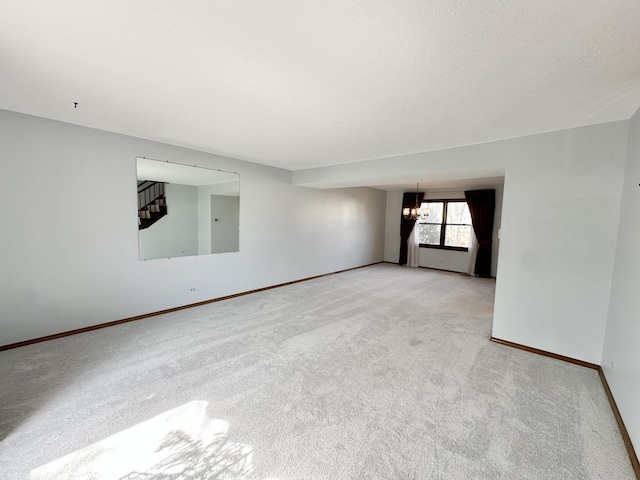 empty room featuring stairs, light colored carpet, baseboards, and a textured ceiling