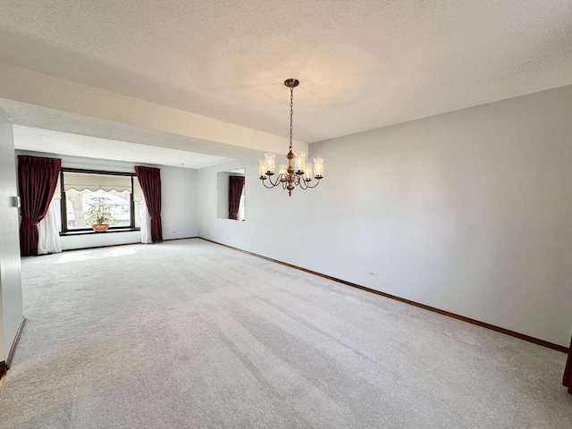 carpeted empty room with a textured ceiling, baseboards, and an inviting chandelier