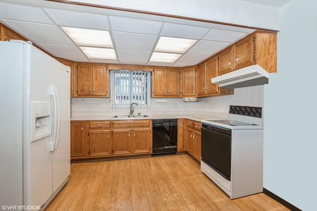 kitchen with brown cabinets, under cabinet range hood, a sink, white appliances, and light wood-style floors