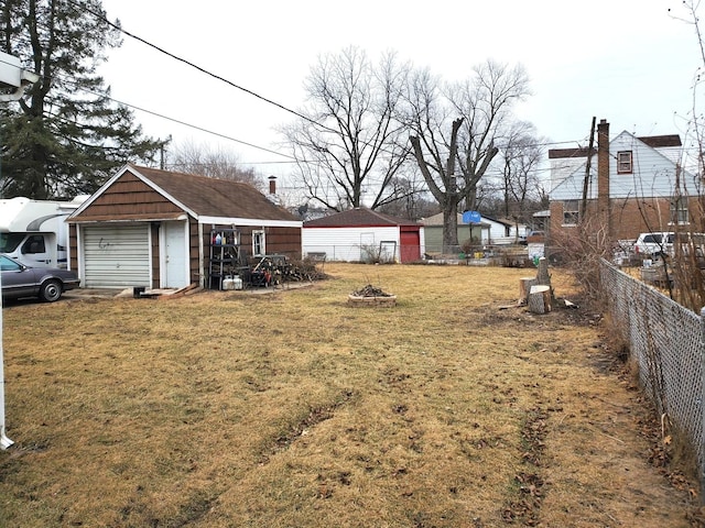 view of yard with a garage, an outdoor fire pit, an outdoor structure, and fence