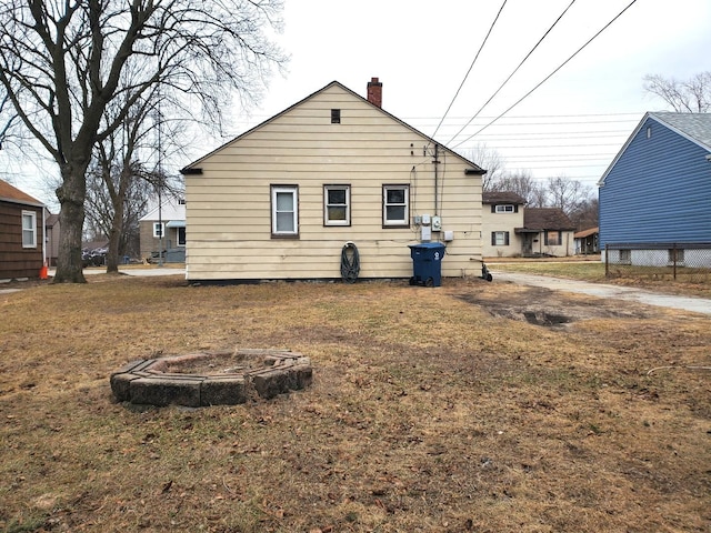 back of property featuring an outdoor fire pit, a yard, and a chimney