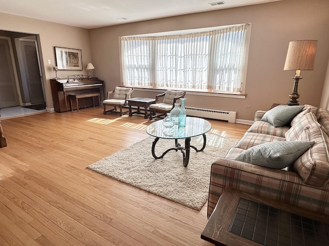 living room with a baseboard heating unit, wood finished floors, visible vents, and baseboards