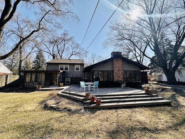 back of property featuring fence, a wooden deck, a lawn, a chimney, and a sunroom