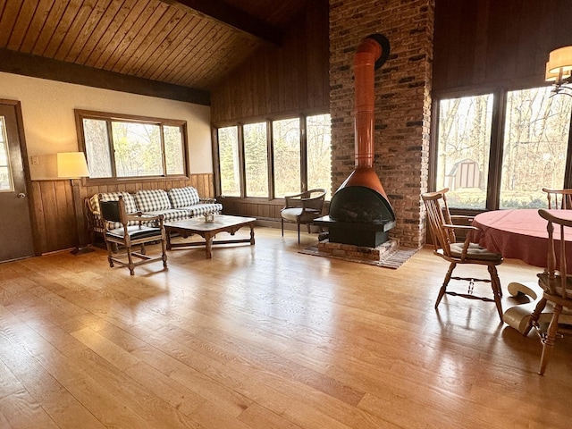 living room featuring beamed ceiling, a wood stove, wood walls, and wainscoting