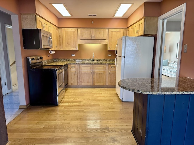 kitchen with light wood finished floors, light brown cabinets, stainless steel appliances, and a sink