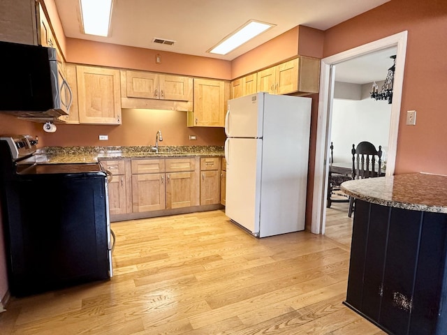 kitchen featuring electric range, light wood-style flooring, light brown cabinets, stainless steel microwave, and freestanding refrigerator