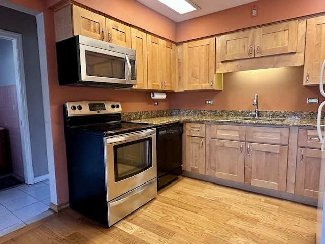 kitchen with dark stone countertops, light wood finished floors, a sink, light brown cabinetry, and stainless steel appliances