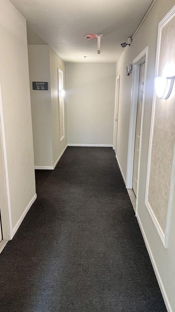 hallway with baseboards and dark carpet