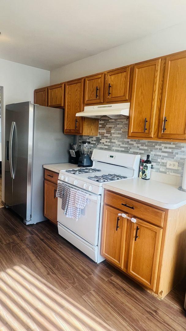 kitchen featuring under cabinet range hood, decorative backsplash, white range with gas stovetop, and stainless steel refrigerator with ice dispenser