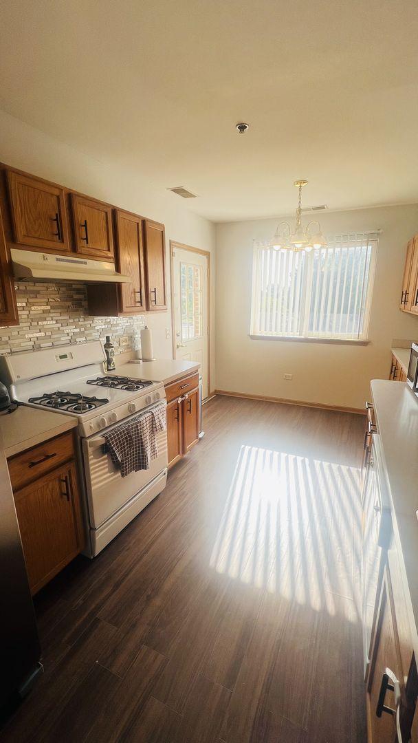 kitchen featuring visible vents, dark wood-type flooring, under cabinet range hood, white gas range oven, and brown cabinets