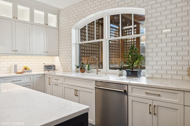 kitchen with backsplash, glass insert cabinets, light stone counters, white cabinetry, and a sink