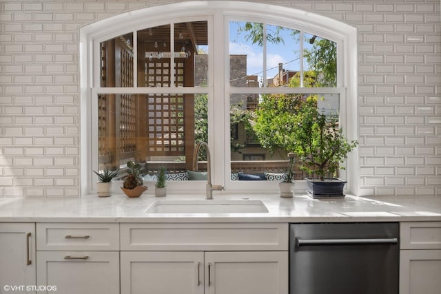 interior space with stainless steel dishwasher, light stone counters, white cabinetry, and a sink