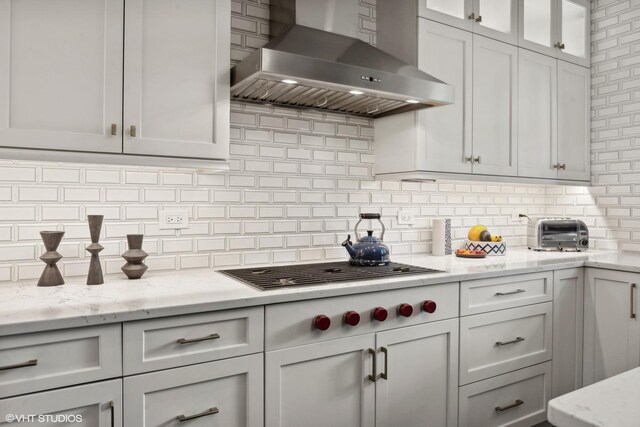 kitchen featuring glass insert cabinets, light stone counters, decorative backsplash, white cabinetry, and wall chimney exhaust hood