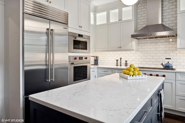 kitchen with wall chimney range hood, light stone counters, tasteful backsplash, and stainless steel appliances