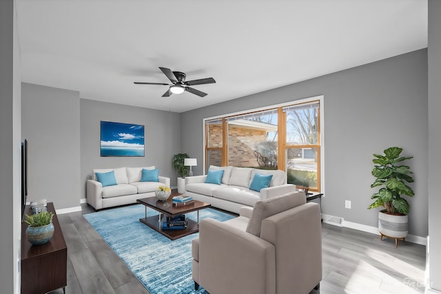 living room featuring light wood-type flooring, visible vents, baseboards, and ceiling fan