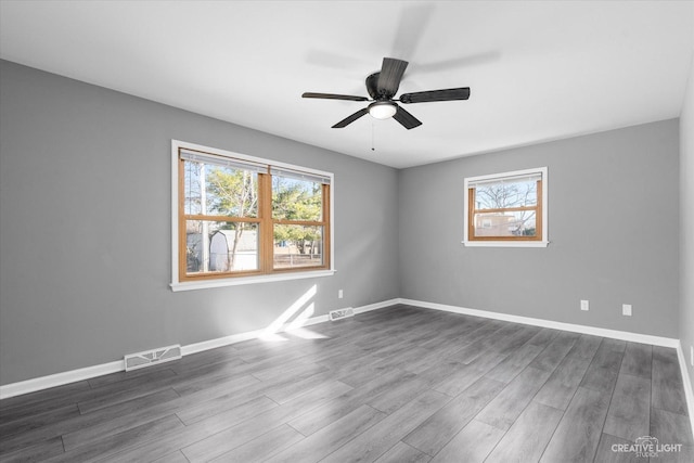 spare room featuring visible vents, dark wood-type flooring, and a healthy amount of sunlight