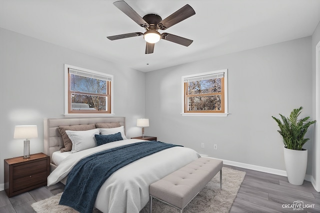 bedroom with multiple windows, a ceiling fan, baseboards, and wood finished floors