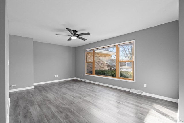 empty room featuring ceiling fan, visible vents, baseboards, and wood finished floors