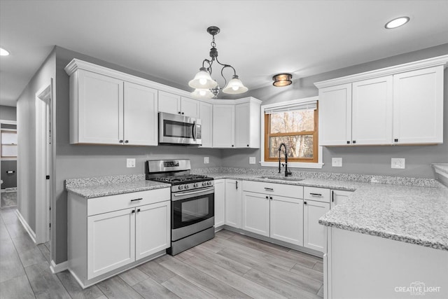 kitchen with wood tiled floor, a sink, stainless steel appliances, pendant lighting, and white cabinetry