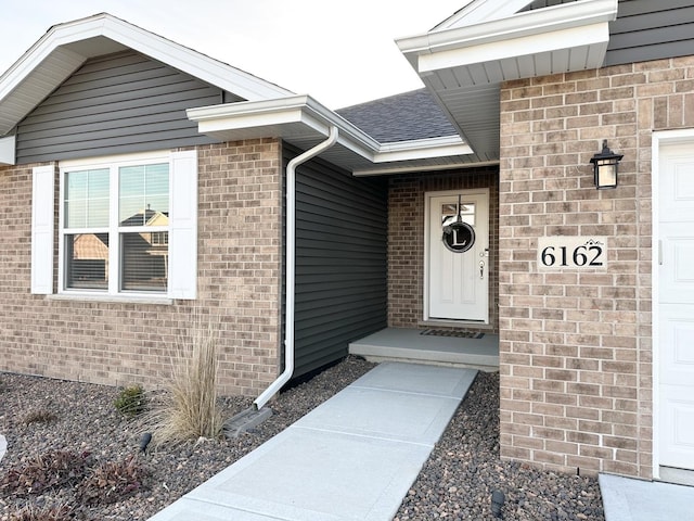 view of exterior entry with brick siding and roof with shingles